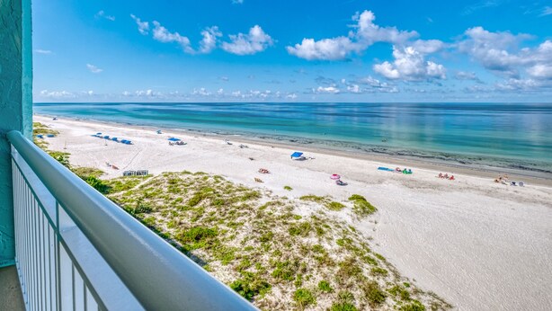 Vista a la playa desde un balcón, con cielo despejado, arena y algunas sombrillas.