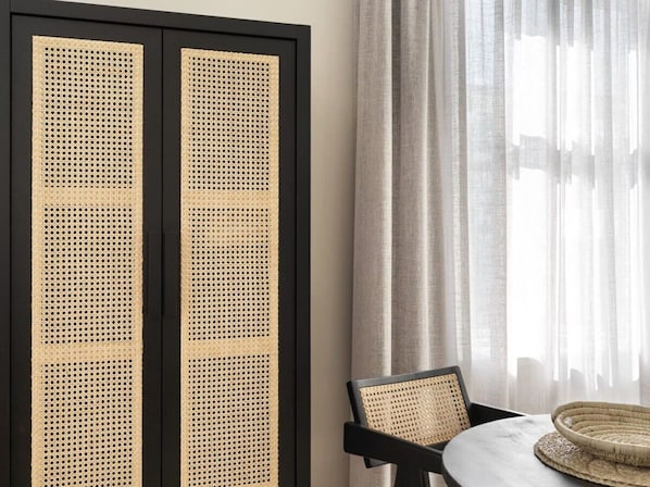 A room with a black-framed woven screen, a round table with a woven chair, and sheer curtains.