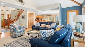 Een ruime woonkamer met een blauwe bank, gestreepe fauteuils, en een eethoek met houten meubels.