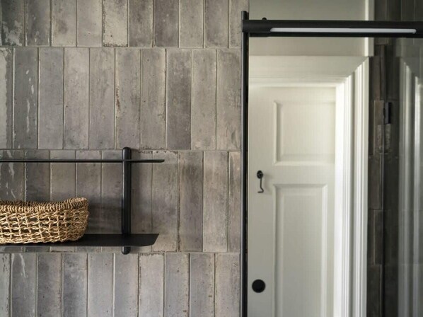 A room with a grey brick wall, a black metal shelf with a woven basket, and a white door.