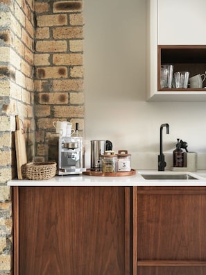 A kitchen with a brick wall, wooden cabinets, a coffee machine, and various kitchen items on the counter. - 46heima // 02 – Deluxe Studio at the best location (Reykjavík)