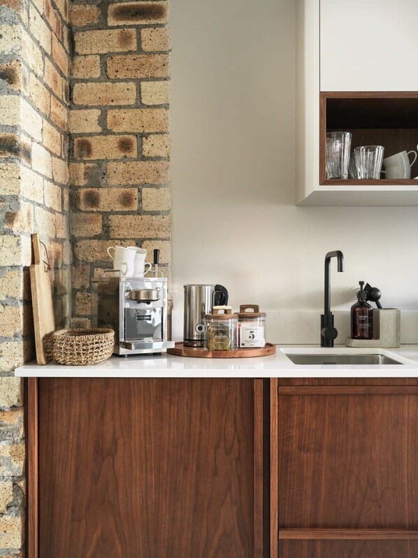 Una cocina con pared de ladrillo, armarios de madera, una cafetera y varios objetos de cocina sobre la encimera.