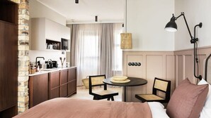A hotel room with a bed, a dining table, chairs, a kitchen area, and a hanging lamp.