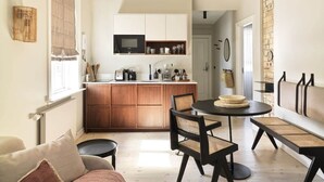 A compact kitchen with wooden cabinets, a dining area with a round table and woven chairs, and a living space with a sofa and a lamp.
