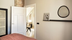 A bedroom with a bed, a white door, a brick wall, a shelf with a picture, and a circular mirror.