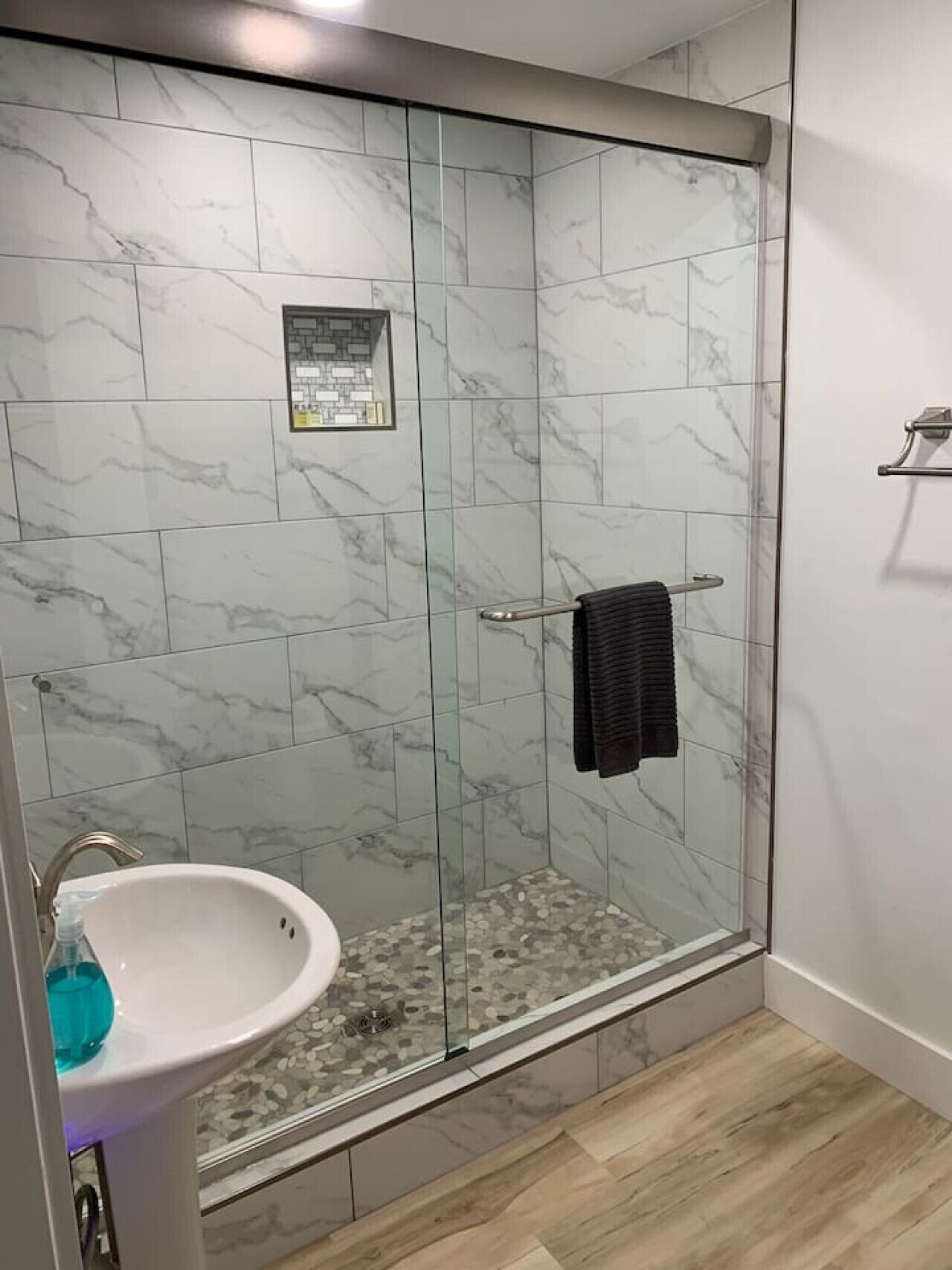 A modern bathroom with a glass-enclosed shower, a white sink, and a tiled floor.