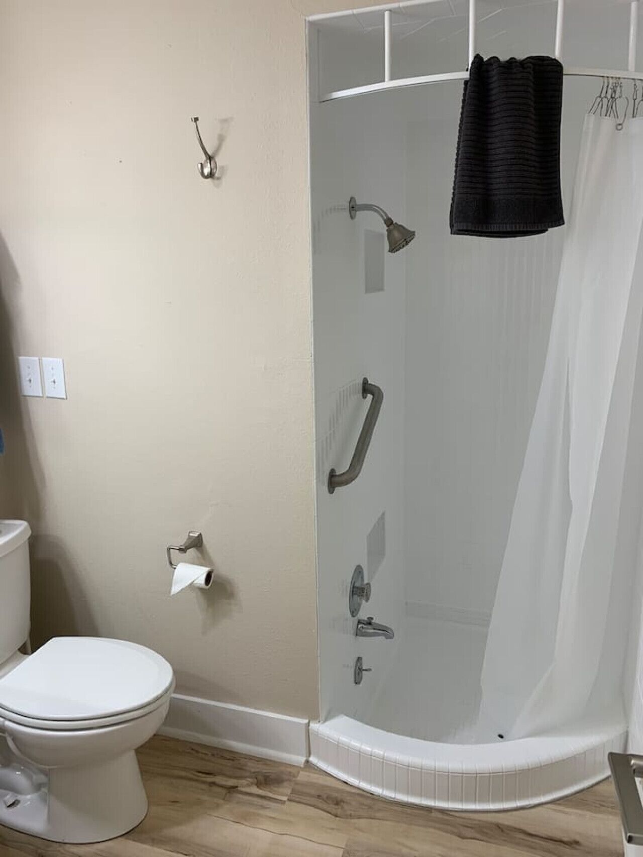 A bathroom with a toilet, a glass-enclosed shower with a towel hanging, and a toilet paper holder on the wall.