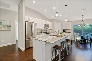 A modern kitchen with white cabinets, stainless steel appliances, and a marble island with bar stools. - 3 bed home w/ beautiful pool in tropical paradise (Naples)