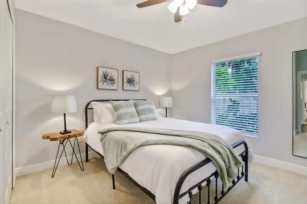 A bedroom with a bed, bedside tables, a ceiling fan, and a window with blinds.