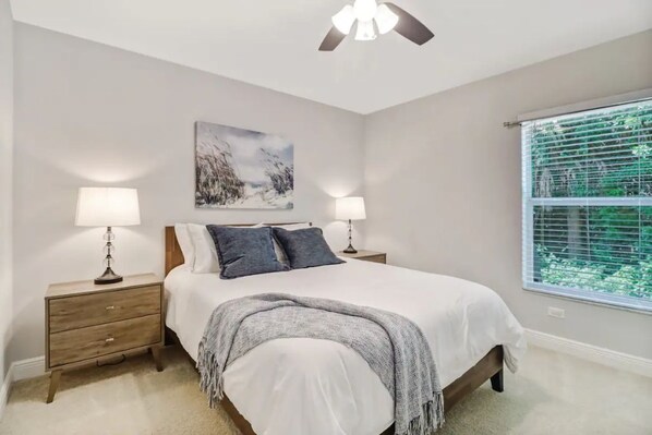 A bedroom with a bed, two bedside tables with lamps, a painting on the wall, and a window with blinds. - 3 bed home w/ beautiful pool in tropical paradise (Naples)