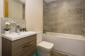 Uma casa de banho moderna com uma sanita, uma banheira, um lavatório branco e uma cómoda de madeira.