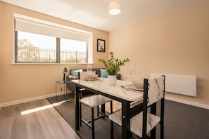 Uma sala de jantar com uma mesa, cadeiras, uma planta e uma janela com vista.