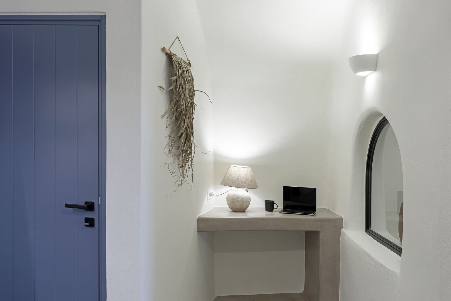 A room with a blue door, a wall-mounted macrame piece, a lamp, a laptop, and a mirror.