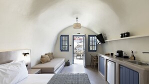 A compact, modern room with a bed, a sofa, a dining area, and a kitchenette. - Acave Santorini Suites (Santorini)