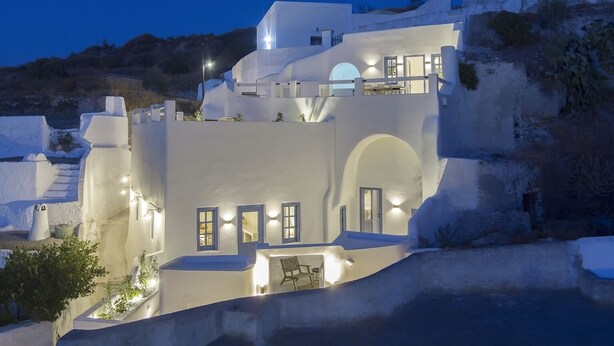 A white, multi-level building with balconies, arched doorways, and outdoor seating areas. - Acave Santorini Suites (Santorini)