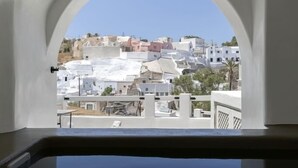 A view through an arched window of a coastal town with white buildings and a clear blue sky. - Acave Santorini Suites (Santorini)