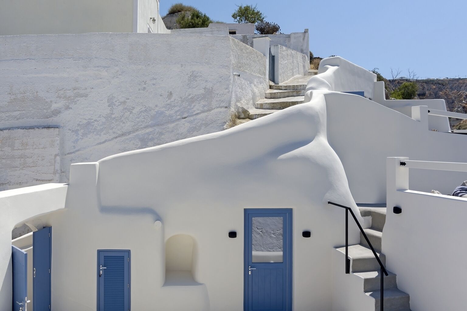 A white building with blue doors and windows, a staircase, and a view of the surrounding landscape.