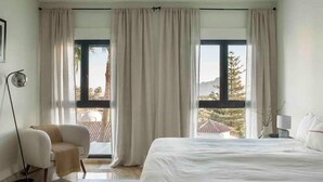 A bedroom with a large bed, two windows with curtains, a chair, and a floor lamp. - Modern Luxury Villa - 5 brm, heated pool, sea views, gym (Calpe)