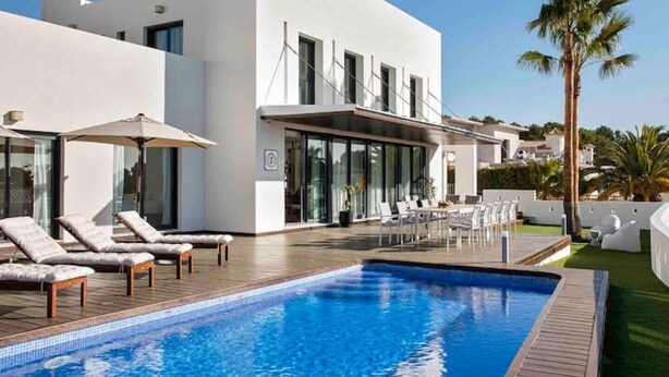 A modern poolside area with lounge chairs and umbrellas, a clear blue pool, and a white building with large windows. - Modern Luxury Villa - 5 brm, heated pool, sea views, gym (Calpe)