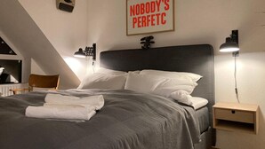 Un dormitorio con cama, mesitas de noche, un escritorio, una silla, una lámpara de pared y un cartel motivacional.