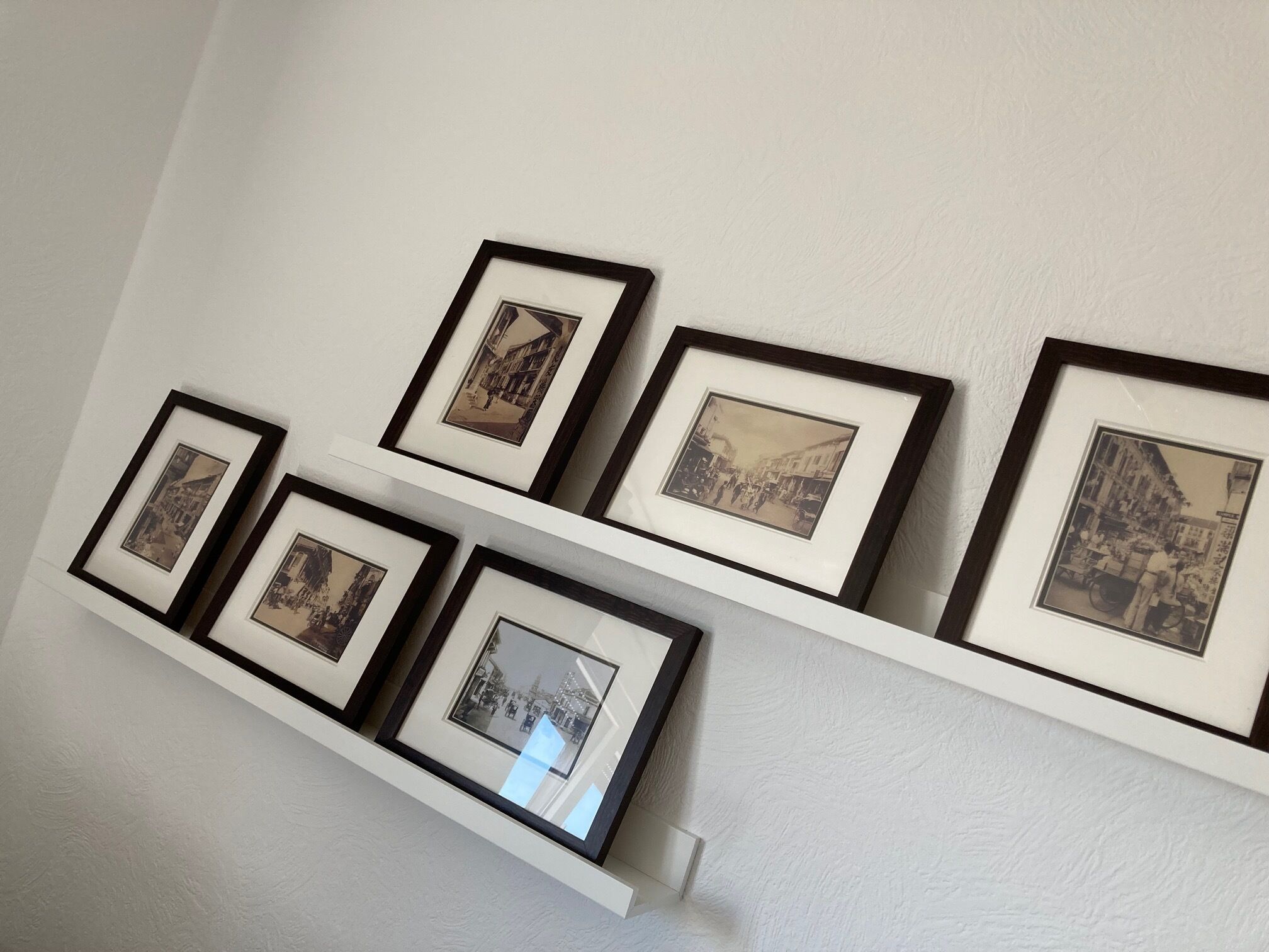 Una pared con una serie de fotografías enmarcadas dispuestas en dos filas sobre un estante blanco.