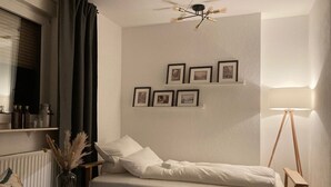 Un dormitorio ordenado con cama, mesita de noche, lámpara y estante con marcos.