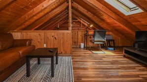 An attic room with wooden walls, a sloped ceiling, a sofa, a table, a chair, a TV, and a skylight. - Log Cabin Retreat w/ Hot Tub, Game Room, Fire Pit (Swanton)