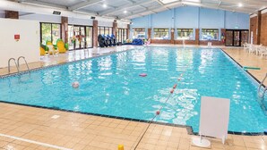 An indoor swimming pool with clear water, a tiled floor, and a roof with skylights.