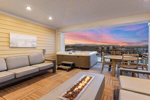 A modern outdoor lounge area with a sofa, hot tub, and a fire feature.