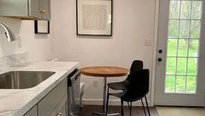 Una cucina con lavello, pensili, un tavolo da pranzo con sedie e una porta che dà su un giardino.