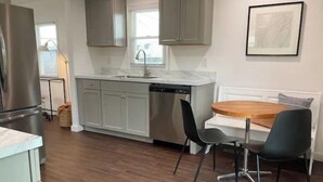 Una cucina moderna con mobili grigi, un frigorifero in acciaio inox, una lavastoviglie e un'area pranzo con un tavolo di legno e sedie nere.