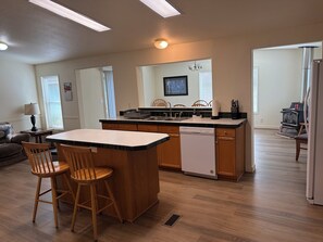 A modern kitchen with a central island, wooden chairs, a dishwasher, and a stove.