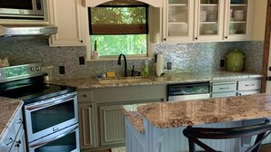 A kitchen with white cabinetry, a wooden ceiling, and a window overlooking greenery.