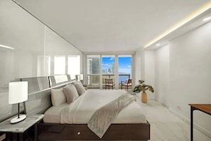 A modern hotel room with a large bed, a bedside table, a lamp, a potted plant, and a view of the city through large windows. - Spacious bay-view balcony stay near Art Miami (Miami)