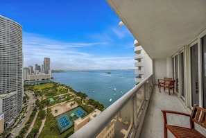 A balcony with a view of a marina, a tennis court, and high-rise buildings.