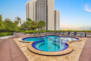 Ein Dachpool mit mehreren Whirlpools, umgeben von Liegestühlen und Palmen.