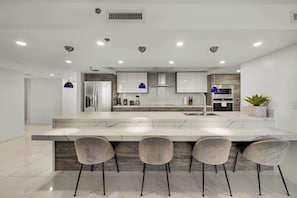 A modern kitchen with a marble island, bar stools, stainless steel appliances, and pendant lighting.