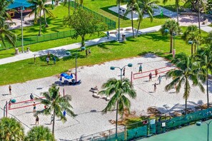 A beach volleyball court with a net, surrounded by palm trees and a grassy area.