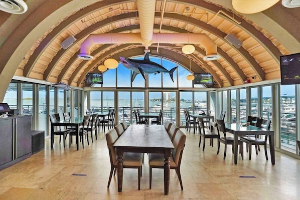 A spacious dining area with a high ceiling and large windows offering a view of the marina.