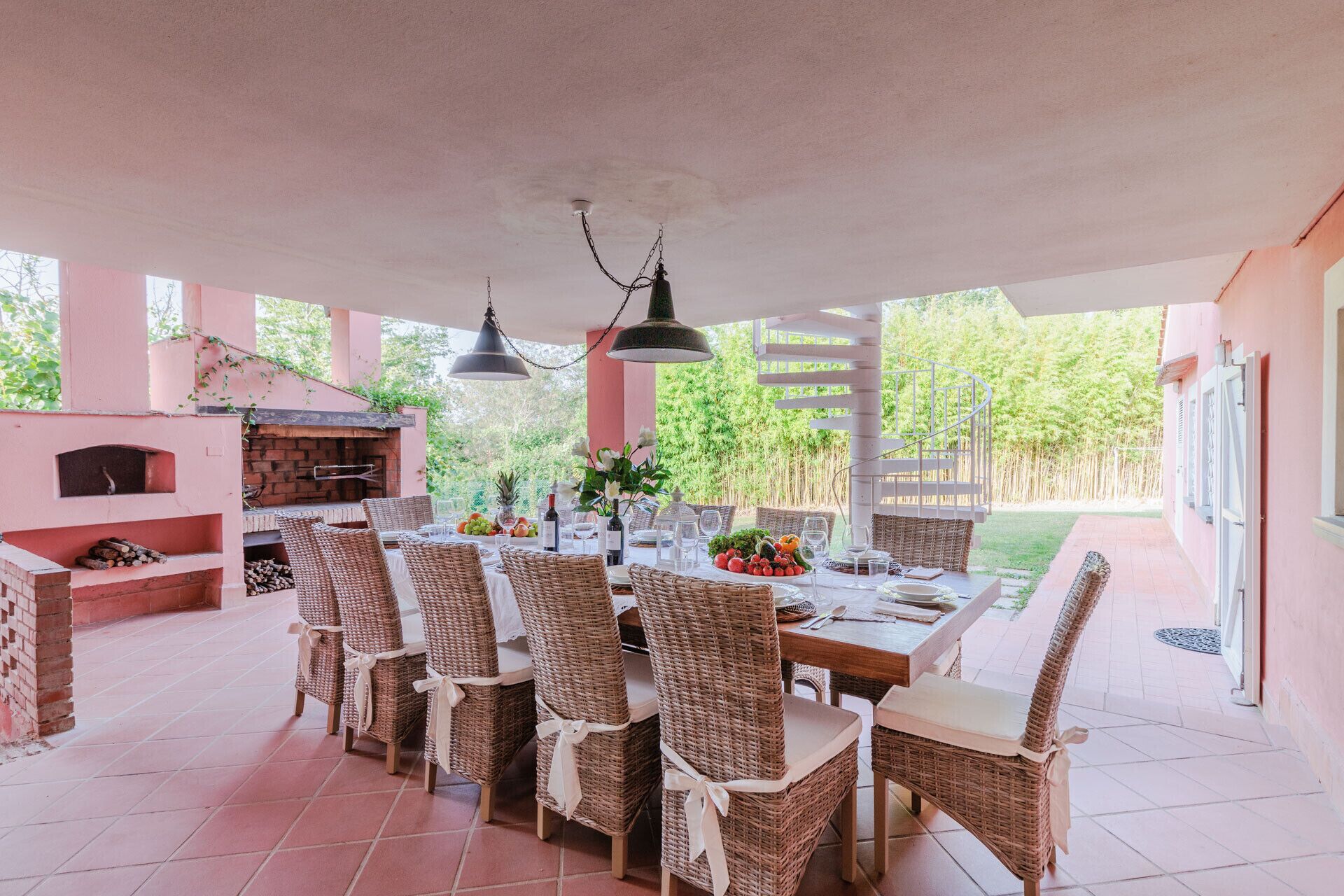 A covered patio with a brick oven, wicker chairs, and a dining table set for six.