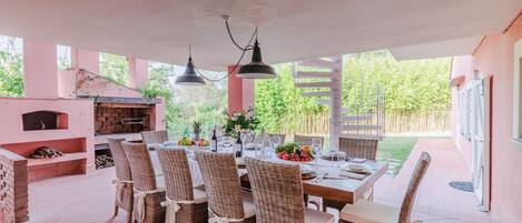 A covered patio with a brick oven, wicker chairs, and a dining table set for six.