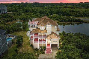 A large, multi-story house with a prominent front porch, a swimming pool, and a view of a lake.
