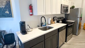 A modern kitchen with white cabinets, stainless steel appliances, a black coffee maker, and a fire extinguisher. - Cozy 2BR Near Airport 4wef (Elizabeth)