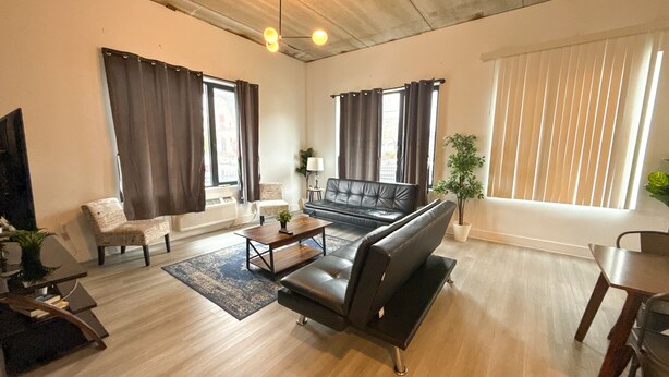 A modern living room with a black leather sofa, a wooden coffee table, a patterned armchair, and a dining table with chairs. - Cozy 2BR Near Airport 4wef (Elizabeth)