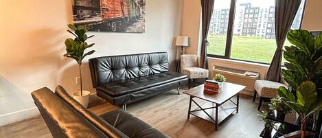 A modern living room with a black leather sofa, a coffee table, and a painting on the wall.