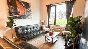 A modern living room with a black leather sofa, a wooden coffee table, and a large window with curtains. - Beautiful 2BR Next to Airport rxfs (Elizabeth)