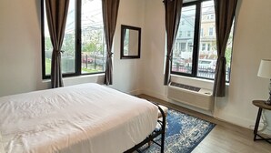 A bedroom with a bed, two windows with curtains, a radiator, and a view of buildings outside. - Beautiful 2BR Next to Airport rxfs (Elizabeth)
