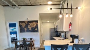 A modern kitchen with white cabinets, stainless steel appliances, and pendant lighting. There is a dining area with a black leather couch and a small table with chairs. - Beautiful 2BR Next to Airport rxfs (Elizabeth)