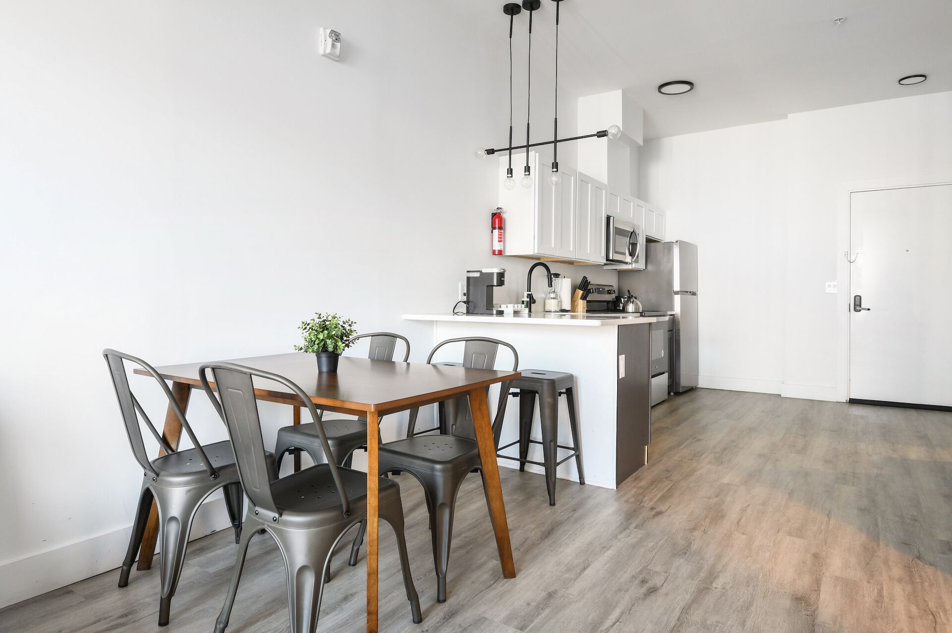 Una cocina moderna con armarios blancos, una isla central y un comedor con sillas de metal y una mesa de madera.