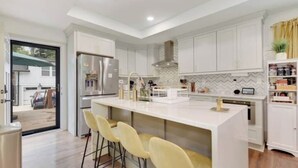 Una cocina moderna con armarios blancos, una isla central con taburetes y vistas al exterior.